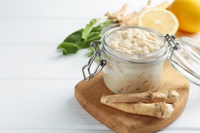 Photo of Tasty horseradish sauce, roots and lemons on white wooden table, closeup. Space for text