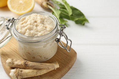 Photo of Tasty horseradish sauce, roots and lemons on white wooden table, closeup. Space for text