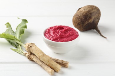 Photo of Tasty horseradish sauce with beetroot, vegetable and roots on white wooden table, closeup