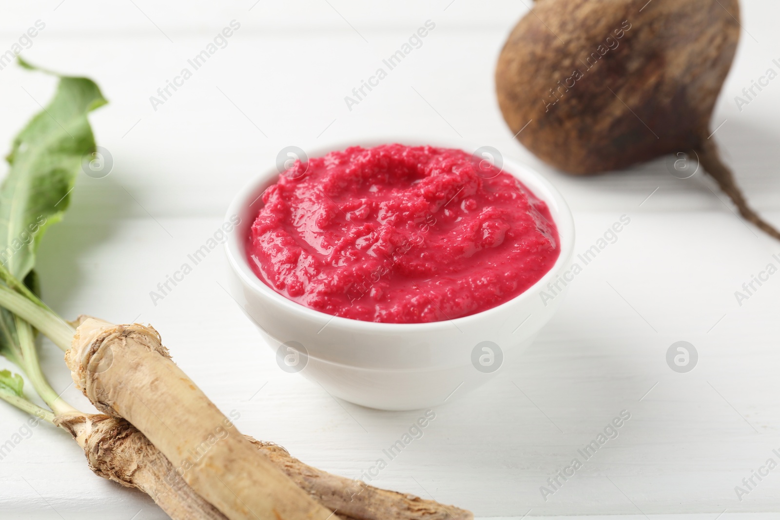 Photo of Tasty horseradish sauce with beetroot, vegetable and roots on white wooden table, closeup