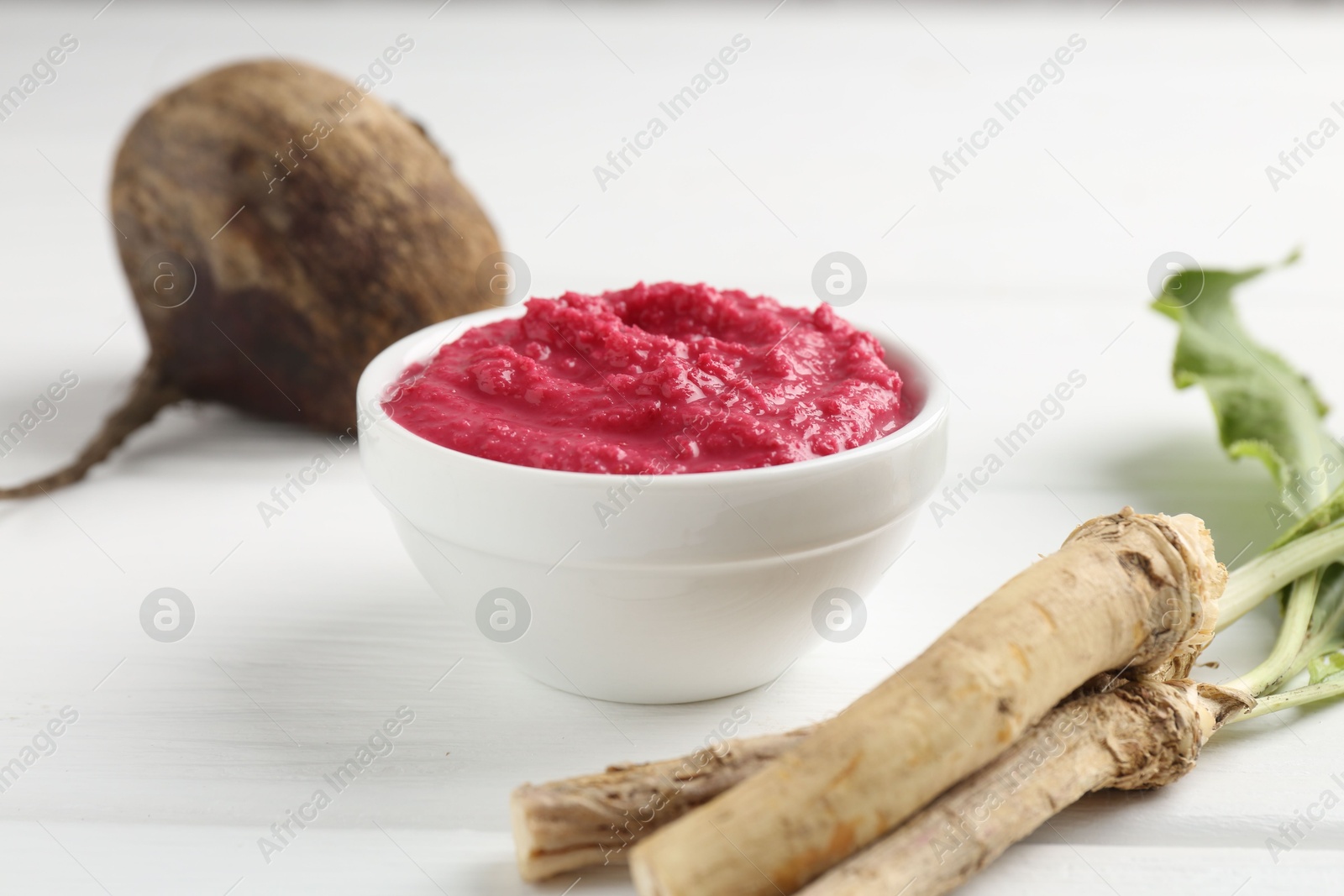 Photo of Tasty horseradish sauce with beetroot, vegetable and roots on white wooden table, closeup