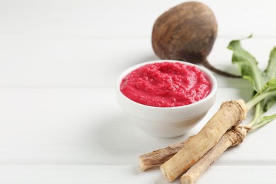 Photo of Tasty horseradish sauce with beetroot, vegetable and roots on white wooden table, closeup. Space for text