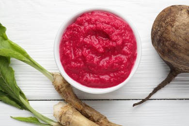 Photo of Tasty horseradish sauce with beetroot, vegetable and roots on white wooden table, flat lay