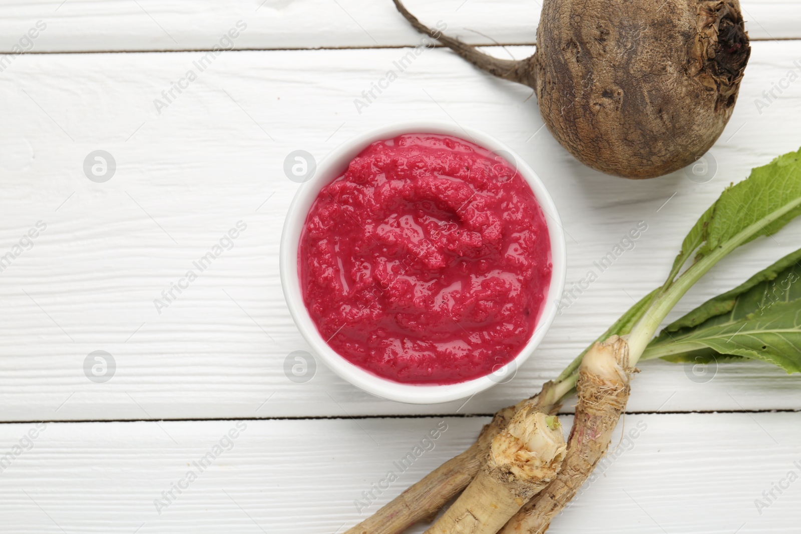 Photo of Tasty horseradish sauce with beetroot, vegetable and roots on white wooden table, flat lay. Space for text