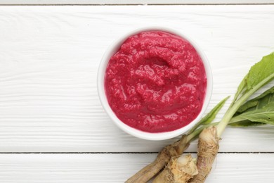 Photo of Tasty horseradish sauce with beetroot, vegetable and roots on white wooden table, flat lay. Space for text