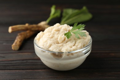Photo of Tasty horseradish sauce with parsley and roots on black wooden table, closeup