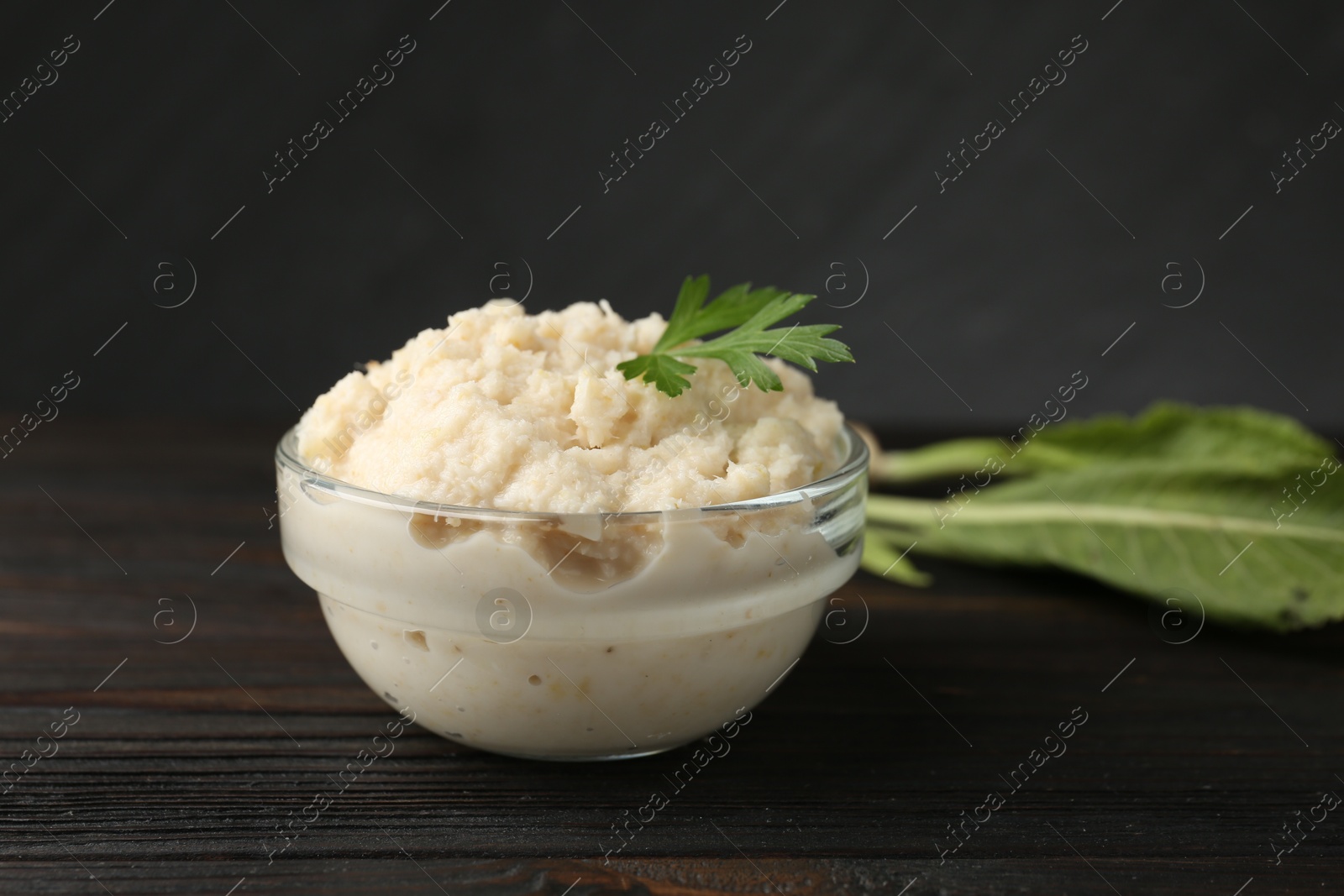Photo of Tasty horseradish sauce with parsley and roots on black wooden table, closeup