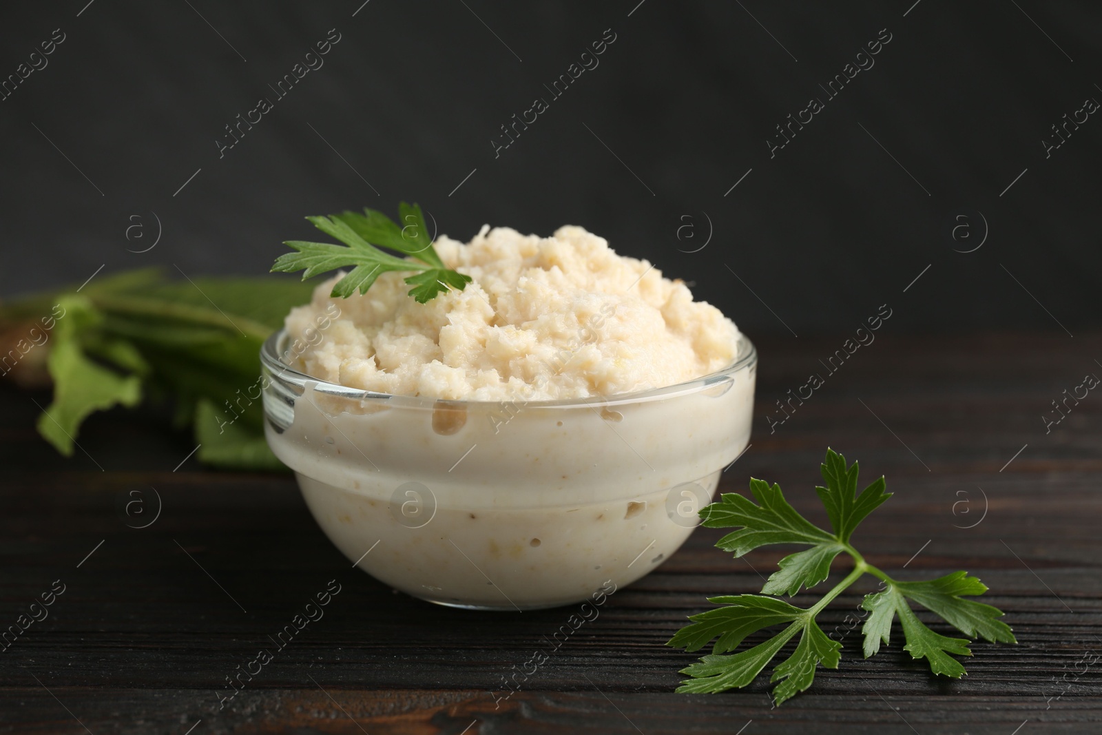 Photo of Tasty horseradish sauce with parsley and roots on black wooden table, closeup
