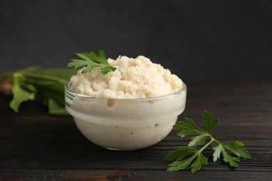 Photo of Tasty horseradish sauce with parsley and roots on black wooden table, closeup