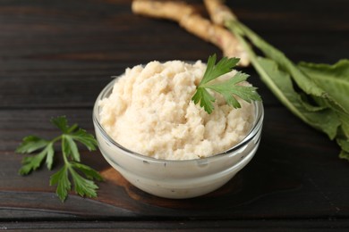 Photo of Tasty horseradish sauce with parsley and roots on black wooden table, closeup