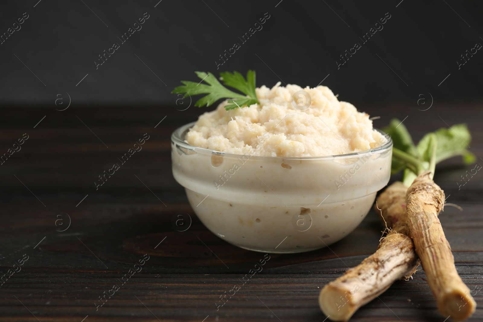 Photo of Tasty horseradish sauce with parsley and roots on black wooden table, closeup. Space for text