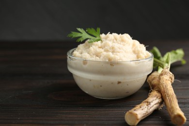 Photo of Tasty horseradish sauce with parsley and roots on black wooden table, closeup. Space for text
