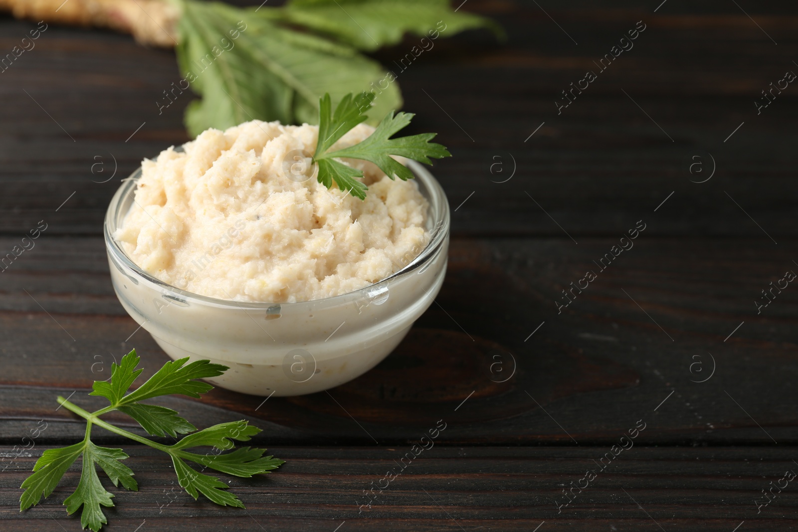 Photo of Tasty horseradish sauce with parsley and roots on black wooden table, closeup. Space for text
