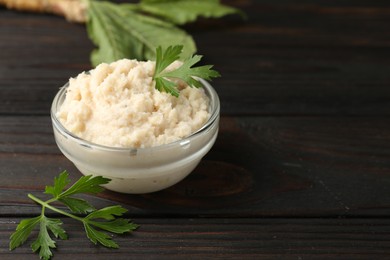 Photo of Tasty horseradish sauce with parsley and roots on black wooden table, closeup. Space for text