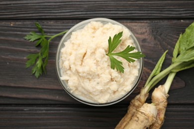 Photo of Tasty horseradish sauce with parsley and roots on black wooden table, flat lay