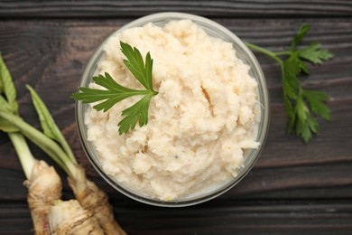 Photo of Tasty horseradish sauce with parsley and roots on black wooden table, flat lay