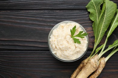 Photo of Tasty horseradish sauce with parsley and roots on black wooden table, flat lay. Space for text