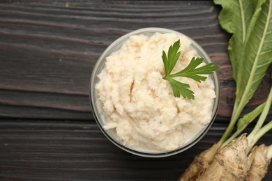 Photo of Tasty horseradish sauce with parsley and roots on black wooden table, flat lay