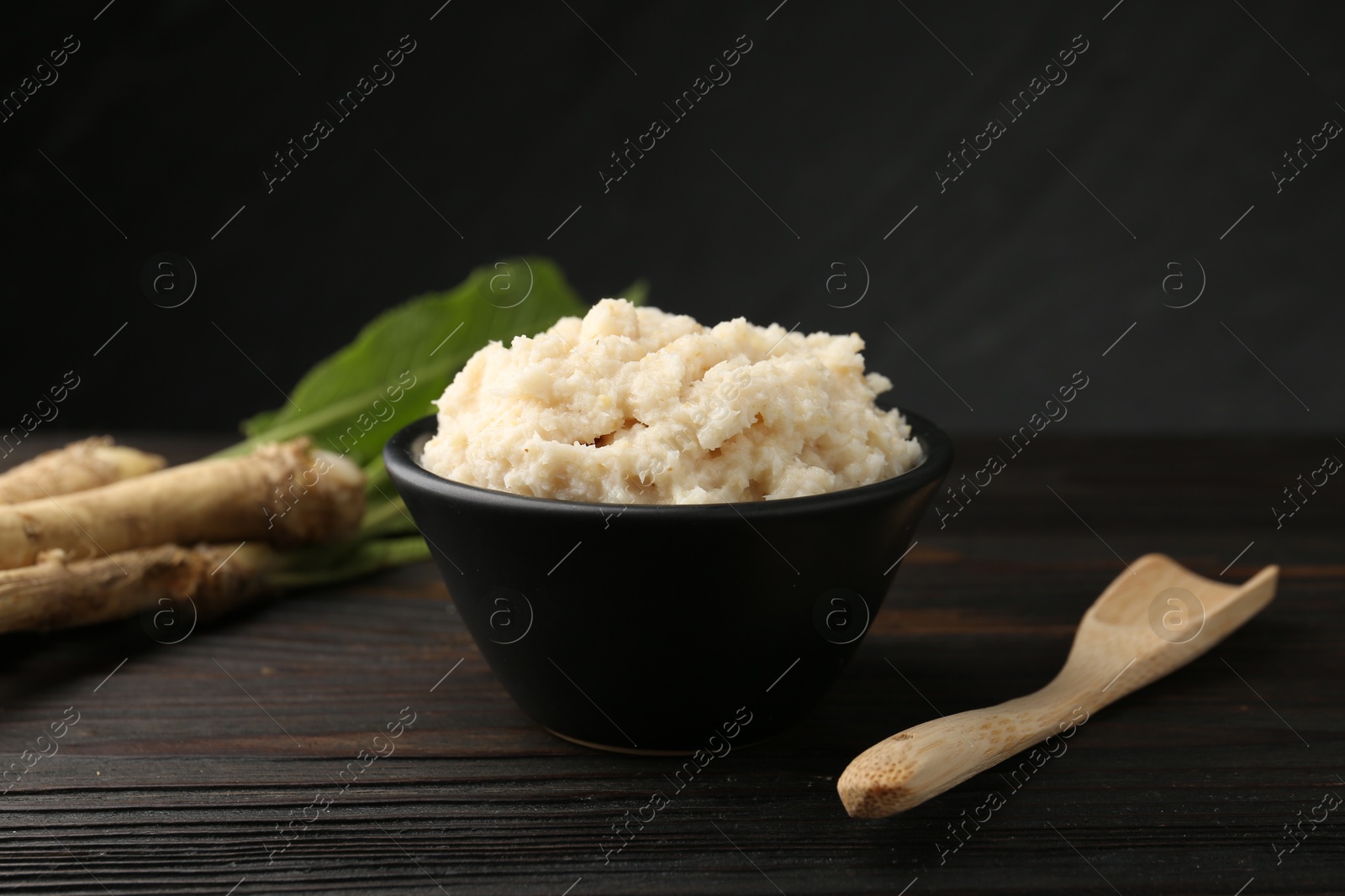 Photo of Tasty horseradish sauce and roots on black wooden table, closeup
