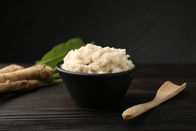 Photo of Tasty horseradish sauce and roots on black wooden table, closeup