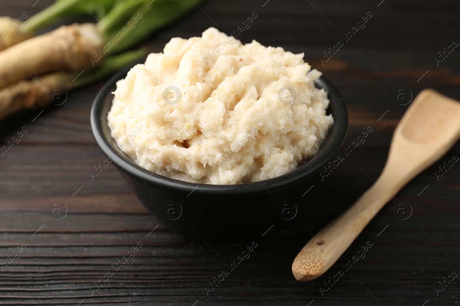 Photo of Tasty horseradish sauce and roots on black wooden table, closeup
