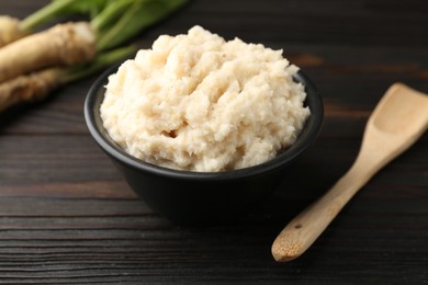 Photo of Tasty horseradish sauce and roots on black wooden table, closeup