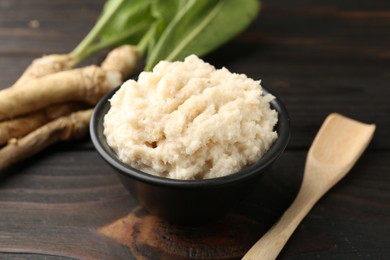 Photo of Tasty horseradish sauce and roots on black wooden table, closeup