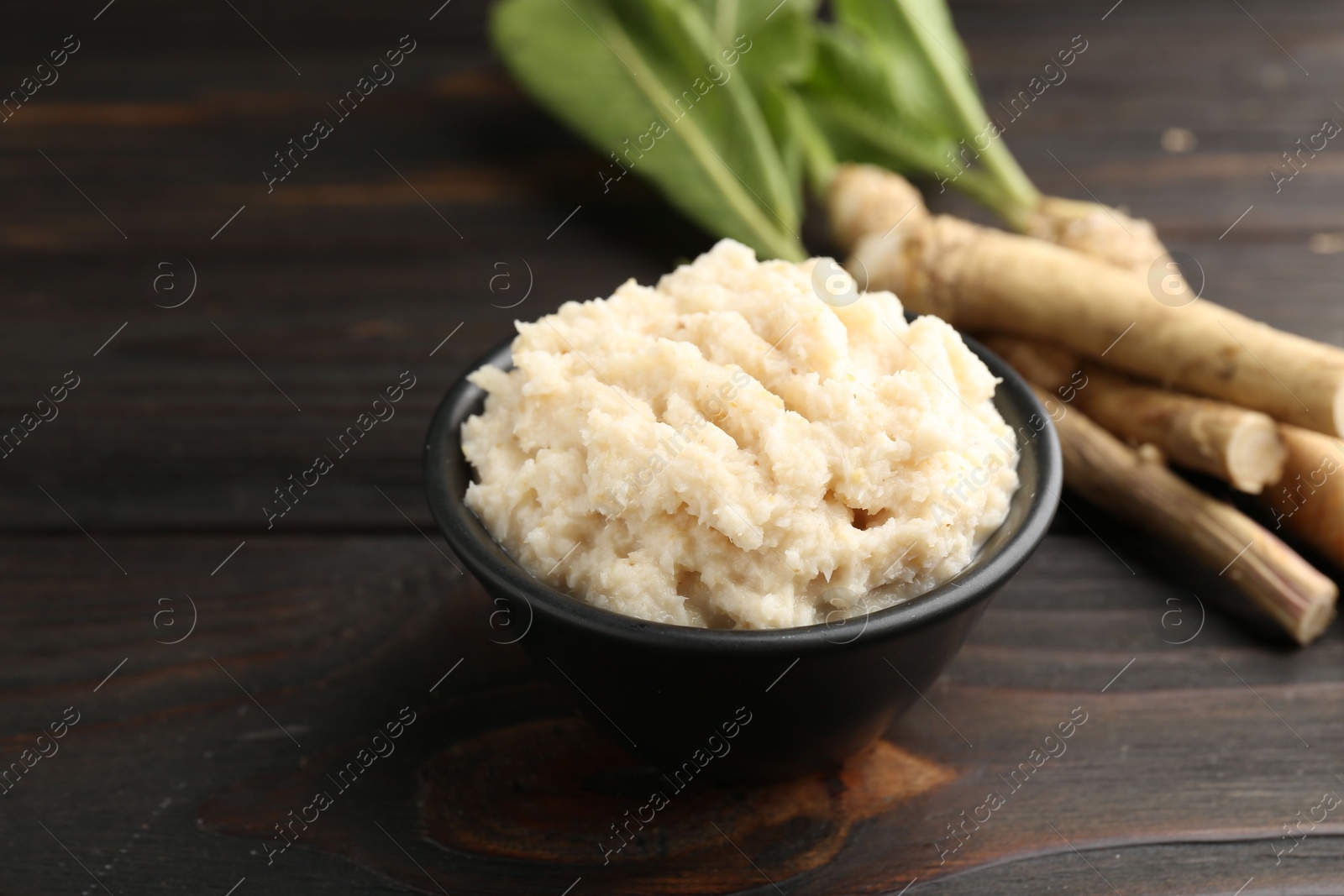 Photo of Tasty horseradish sauce and roots on black wooden table, closeup
