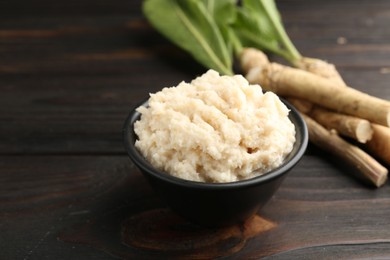 Photo of Tasty horseradish sauce and roots on black wooden table, closeup