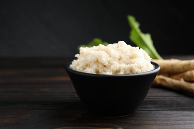 Photo of Tasty horseradish sauce and roots on black wooden table, closeup. Space for text