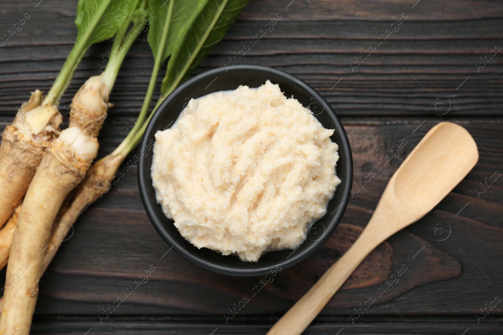 Photo of Tasty horseradish sauce and roots on black wooden table, flat lay
