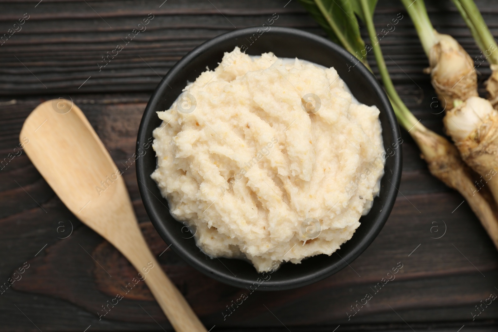 Photo of Tasty horseradish sauce and roots on black wooden table, flat lay