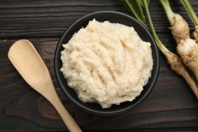 Photo of Tasty horseradish sauce and roots on black wooden table, flat lay