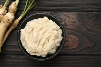 Photo of Tasty horseradish sauce and roots on black wooden table, flat lay. Space for text