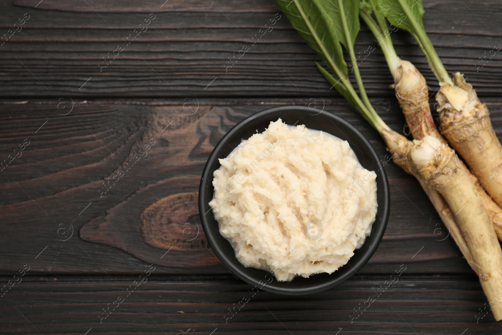 Photo of Tasty horseradish sauce and roots on black wooden table, flat lay. Space for text
