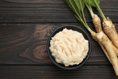 Photo of Tasty horseradish sauce and roots on black wooden table, flat lay. Space for text