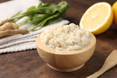 Photo of Tasty horseradish sauce and roots on wooden table, closeup