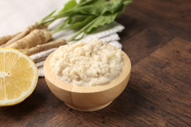 Photo of Tasty horseradish sauce and roots on wooden table, closeup