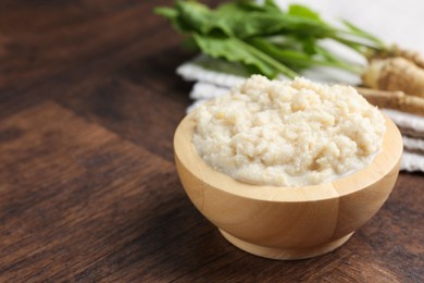 Photo of Tasty horseradish sauce and roots on wooden table, closeup. Space for text