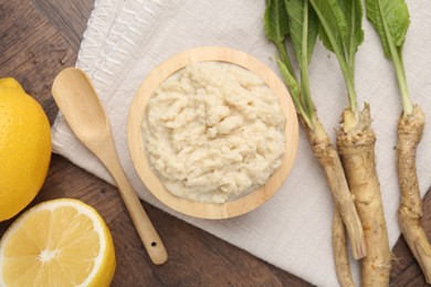 Photo of Tasty horseradish sauce, lemons and roots on wooden table, flat lay