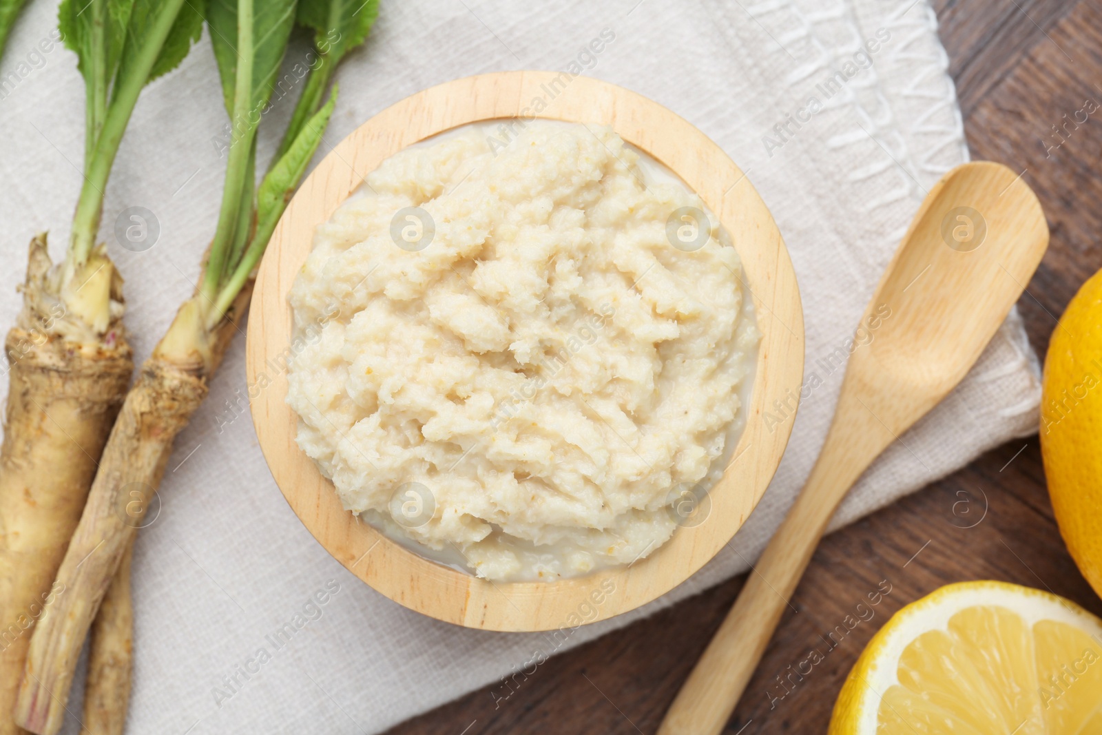 Photo of Tasty horseradish sauce, lemons and roots on wooden table, flat lay