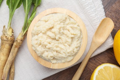 Photo of Tasty horseradish sauce, lemons and roots on wooden table, flat lay