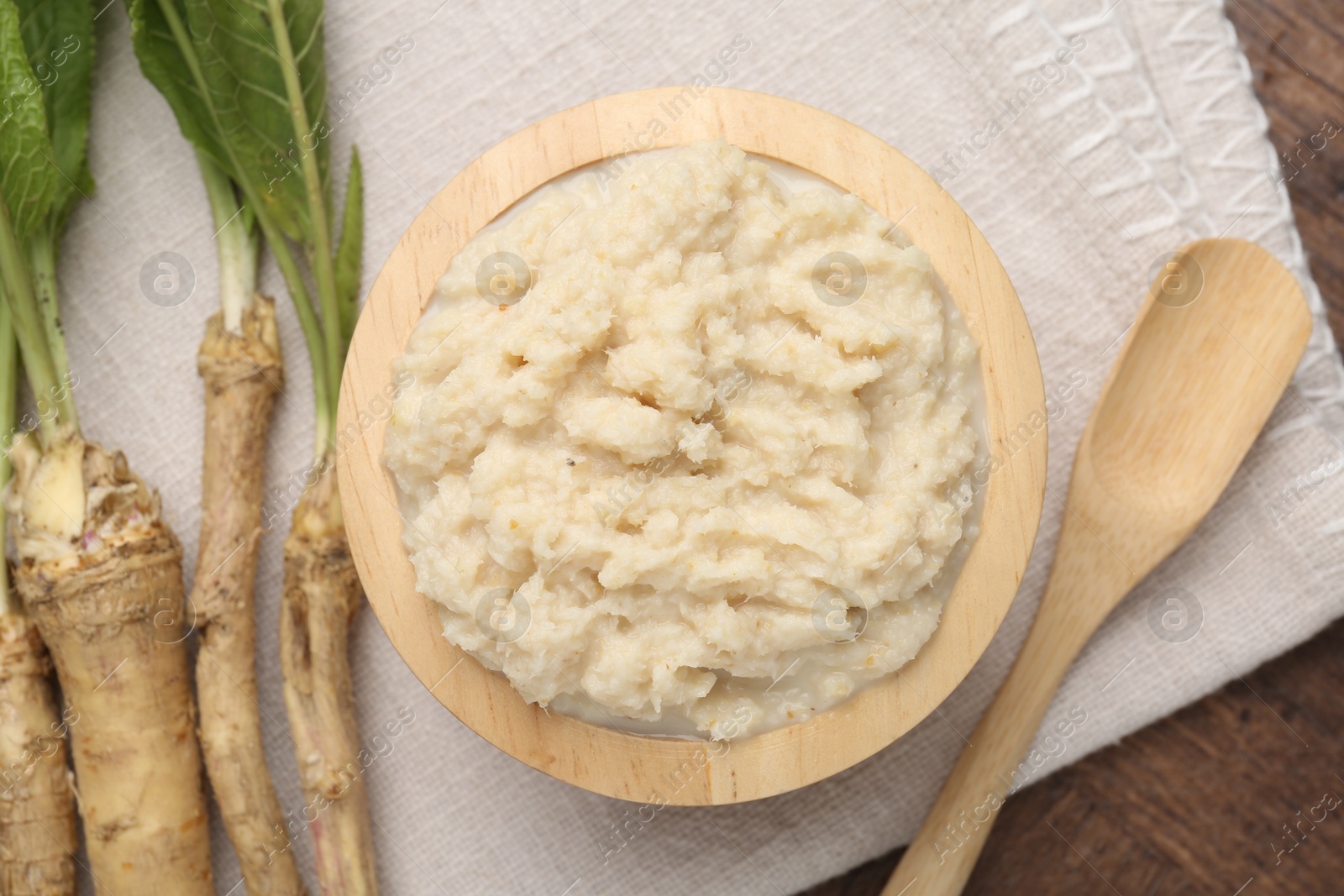 Photo of Tasty horseradish sauce and roots on wooden table, flat lay