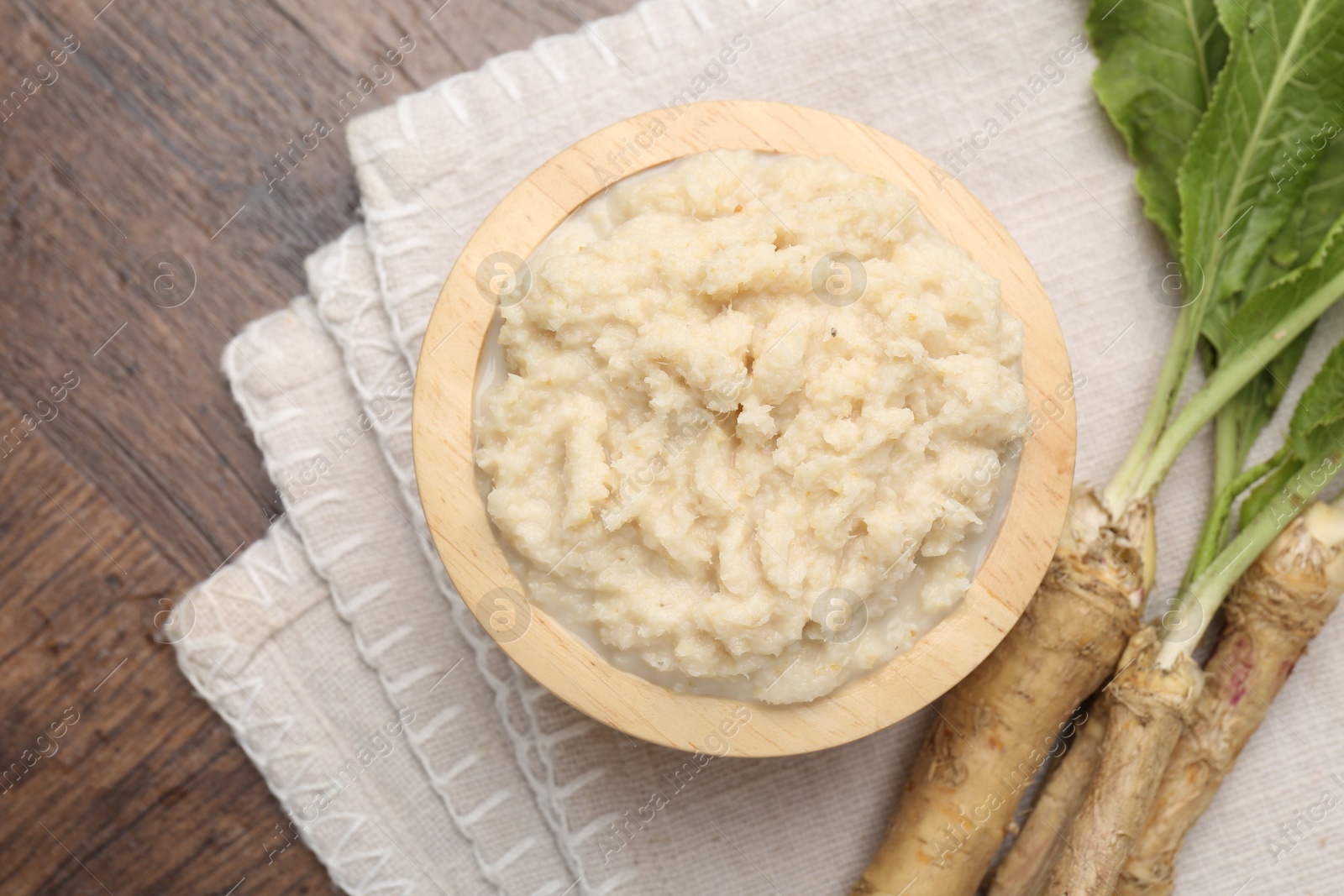Photo of Tasty horseradish sauce and roots on wooden table, flat lay