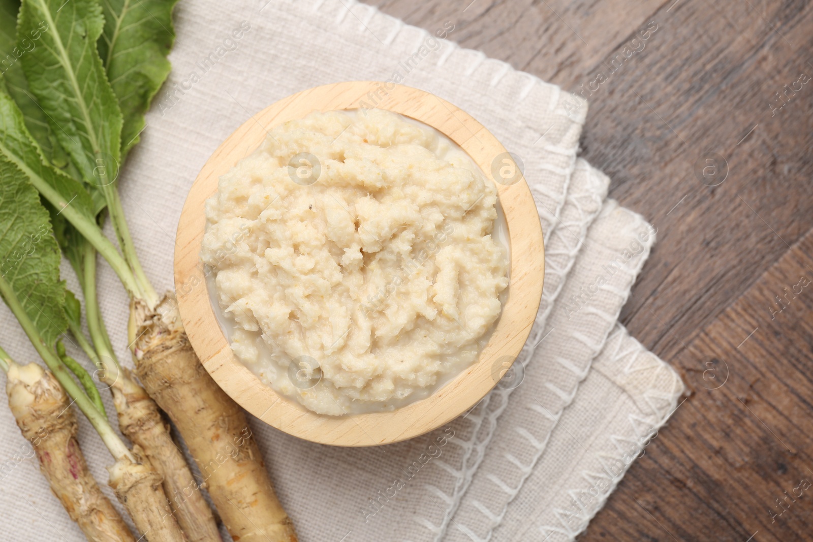 Photo of Tasty horseradish sauce and roots on wooden table, flat lay