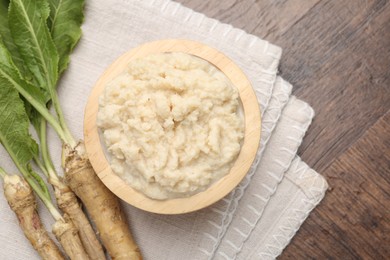 Photo of Tasty horseradish sauce and roots on wooden table, flat lay