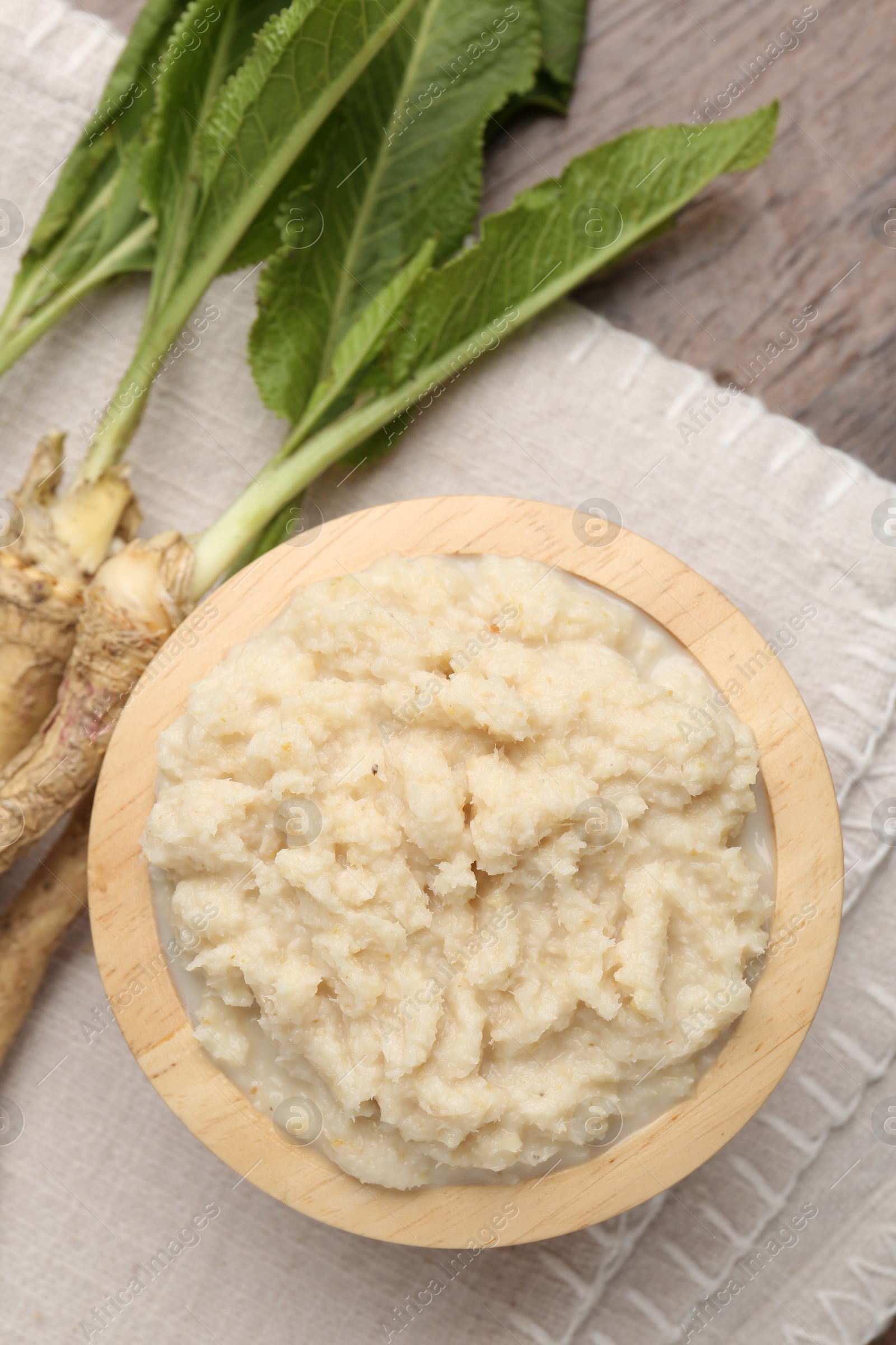 Photo of Tasty horseradish sauce and roots on wooden table, flat lay