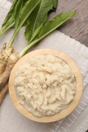 Photo of Tasty horseradish sauce and roots on wooden table, flat lay