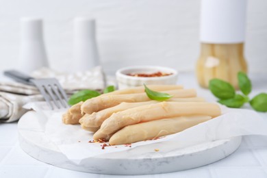Photo of Pickled asparagus spears with spices and basil on white table, closeup