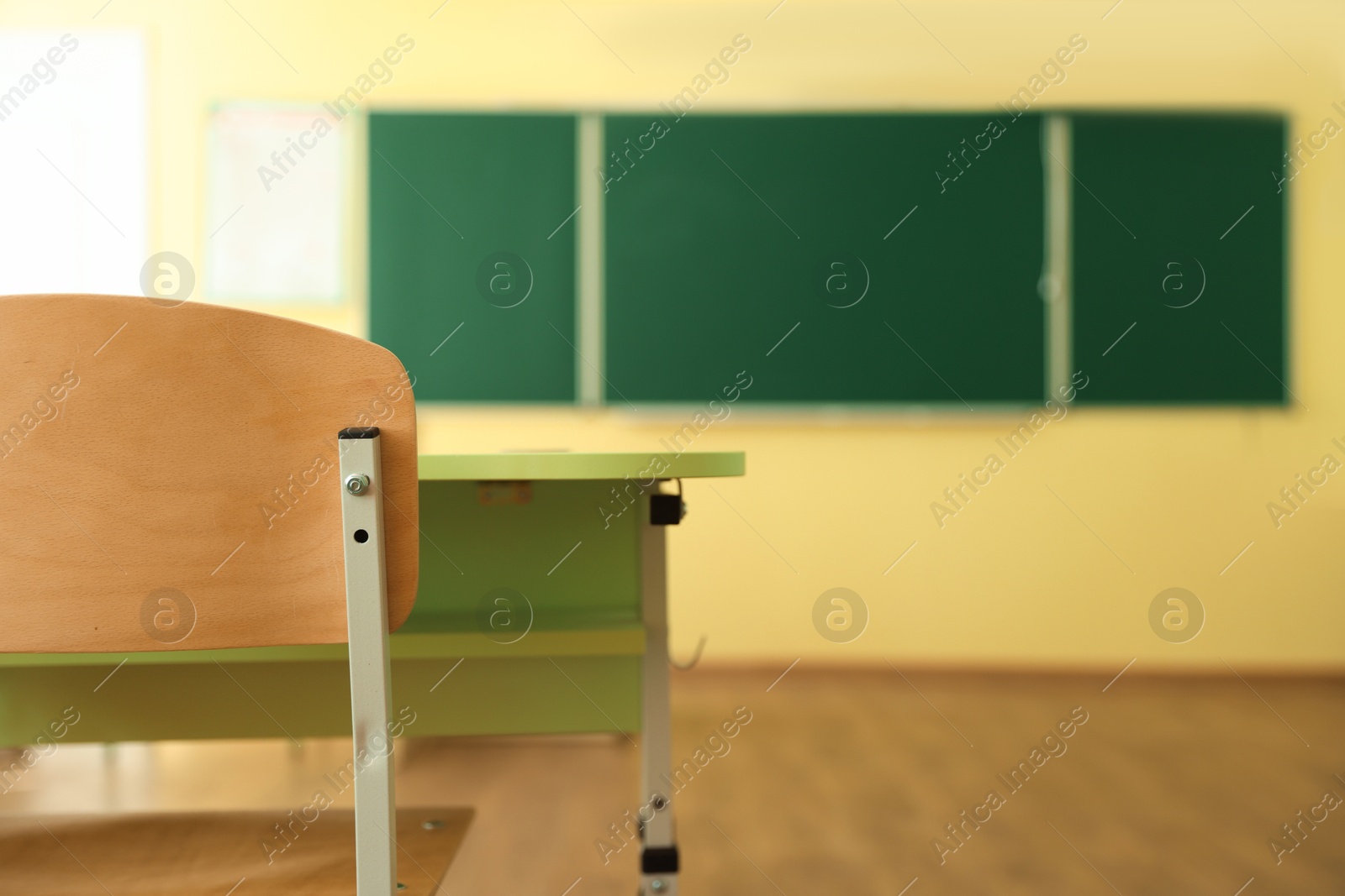 Photo of Desk with chair and green chalkboard in classroom, selective focus